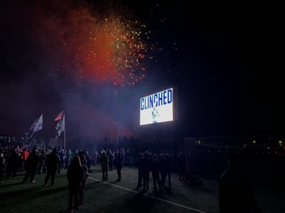 A video board displaying "CLINCHED" in front of a large contingent of STLFC Supporters on the pitch with fireworks in the background.